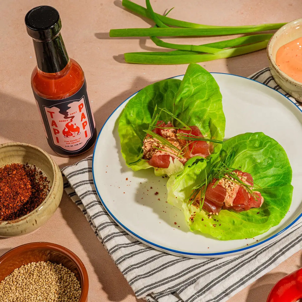 Plated tuna lettuce wraps with a bottle of Tapi Papi hot sauce on a wooden surface.